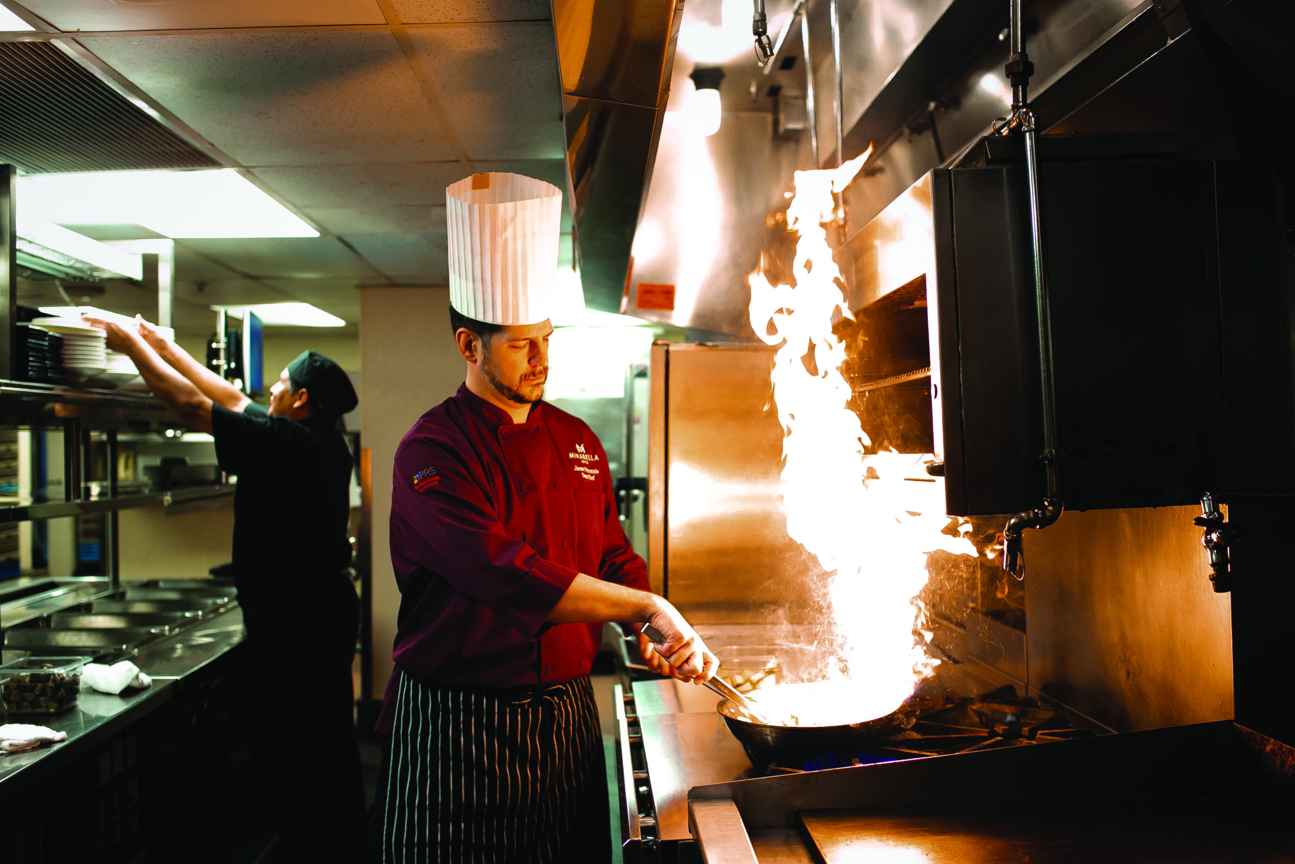 Cinematic photo of a chef flipping a wok, whose contents are on fire.