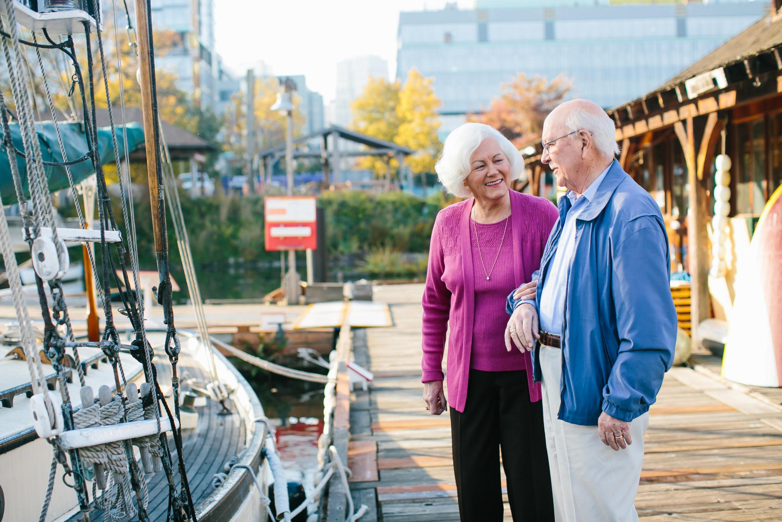 Two Mirabella Seattle residents smile in front of a boat at the dock.