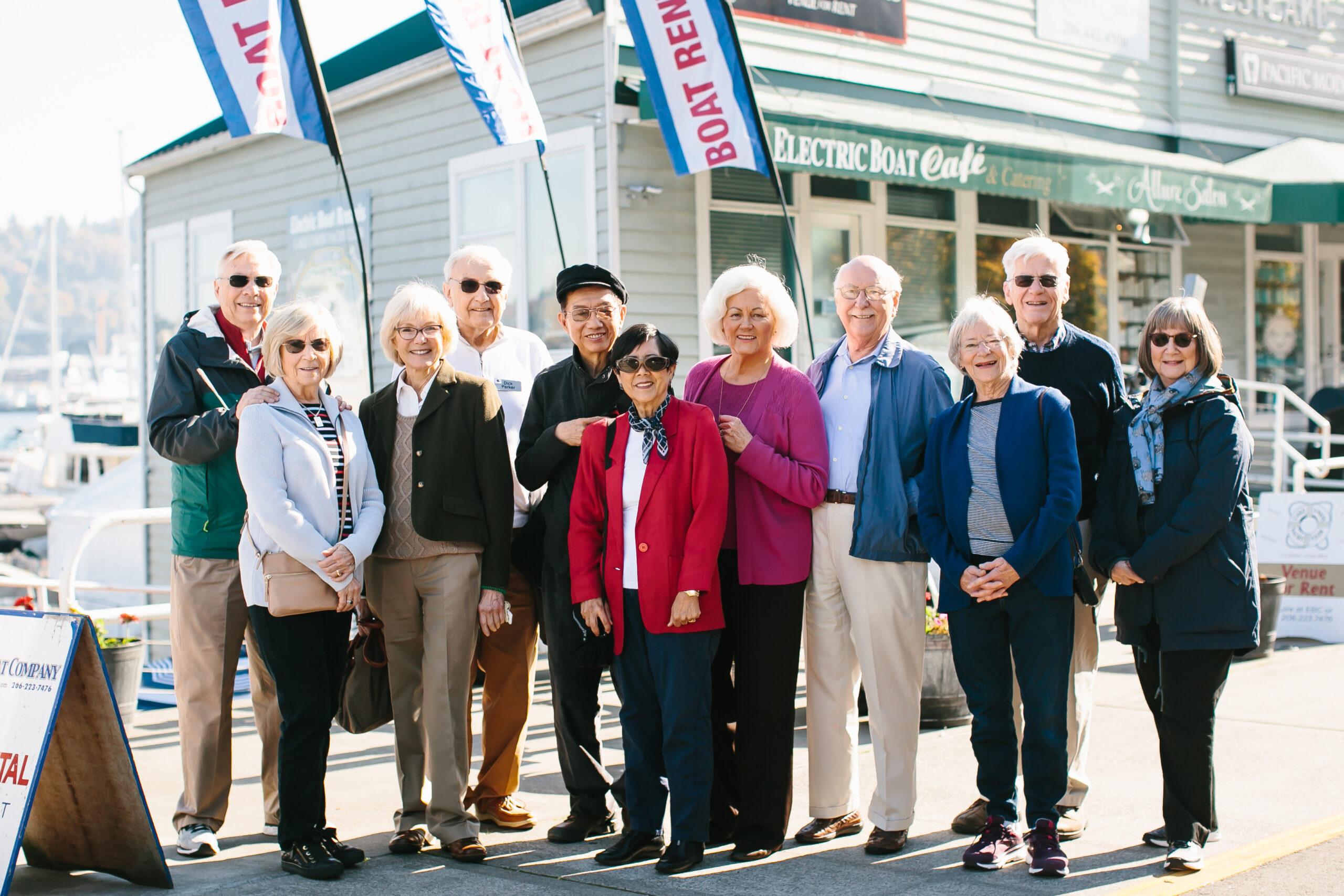 A group of Mirabella Seattle residents gather for a group photo in front of a boat rental at the marina.